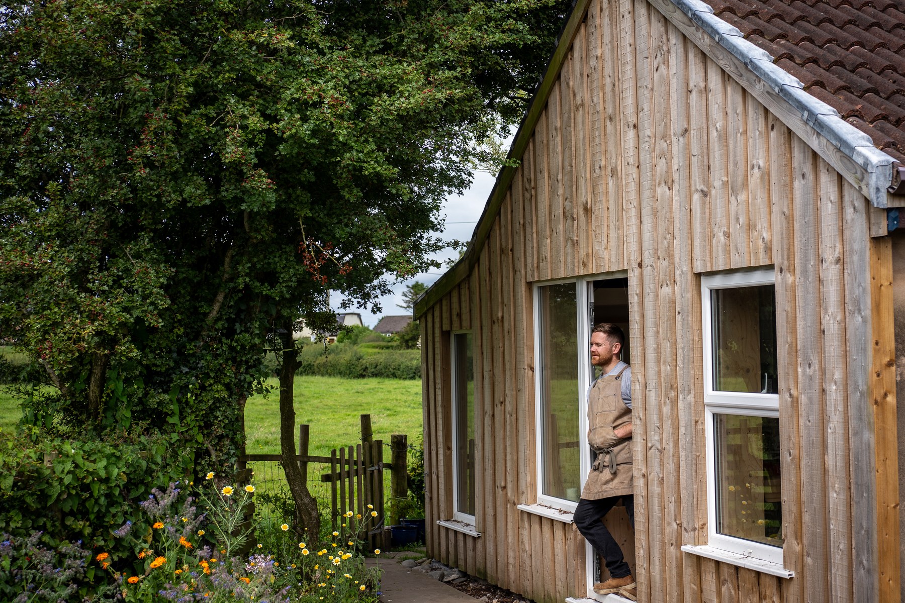 The workshop from outside — timber clad, Robert Scott in the doorway, fields beyond.